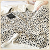 A cream and black leopard print jacquard knit throw blanket draped over a person in bed.