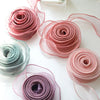 A collection of silky organza ribbon rolls in shades of pink and purple, displayed on a white surface.