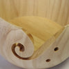 A light wooden yarn bowl with a spiral design used for crochet and knitting organization.