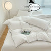 A white duvet cover set with a soft, quilted texture is displayed on a bed, next to a window.