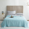 A light blue ice silk cooling comforter is laid on a bed with a neutral upholstered headboard.