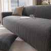 A dark gray protective anti-scratch sofa slipcover with textured fabric and a beige throw pillow on a light rug.