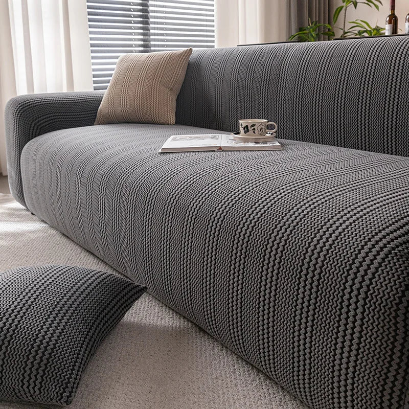 A dark gray protective anti-scratch sofa slipcover with textured fabric and a beige throw pillow on a light rug.