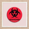 A red circular pin featuring a black biohazard symbol on a light pink background.