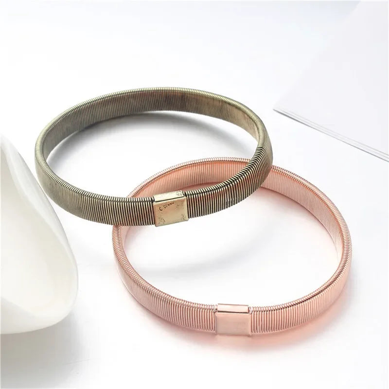 Two adjustable metal sleeve garters for men, one silver and one rose gold, displayed on a white surface.