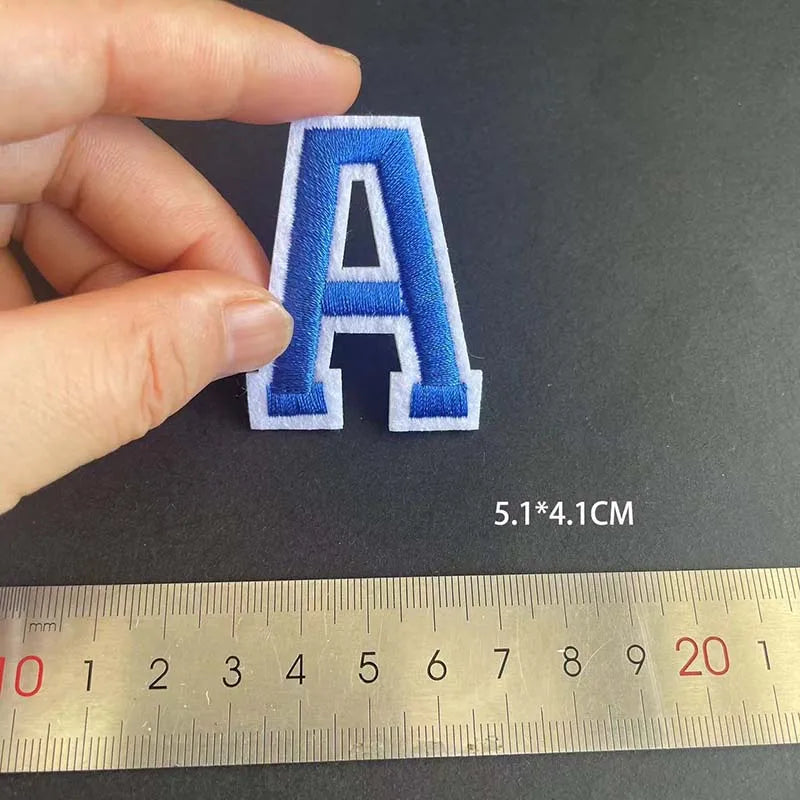 A letter A embroidery iron-on patch in blue and white on a black background, measured by a ruler.