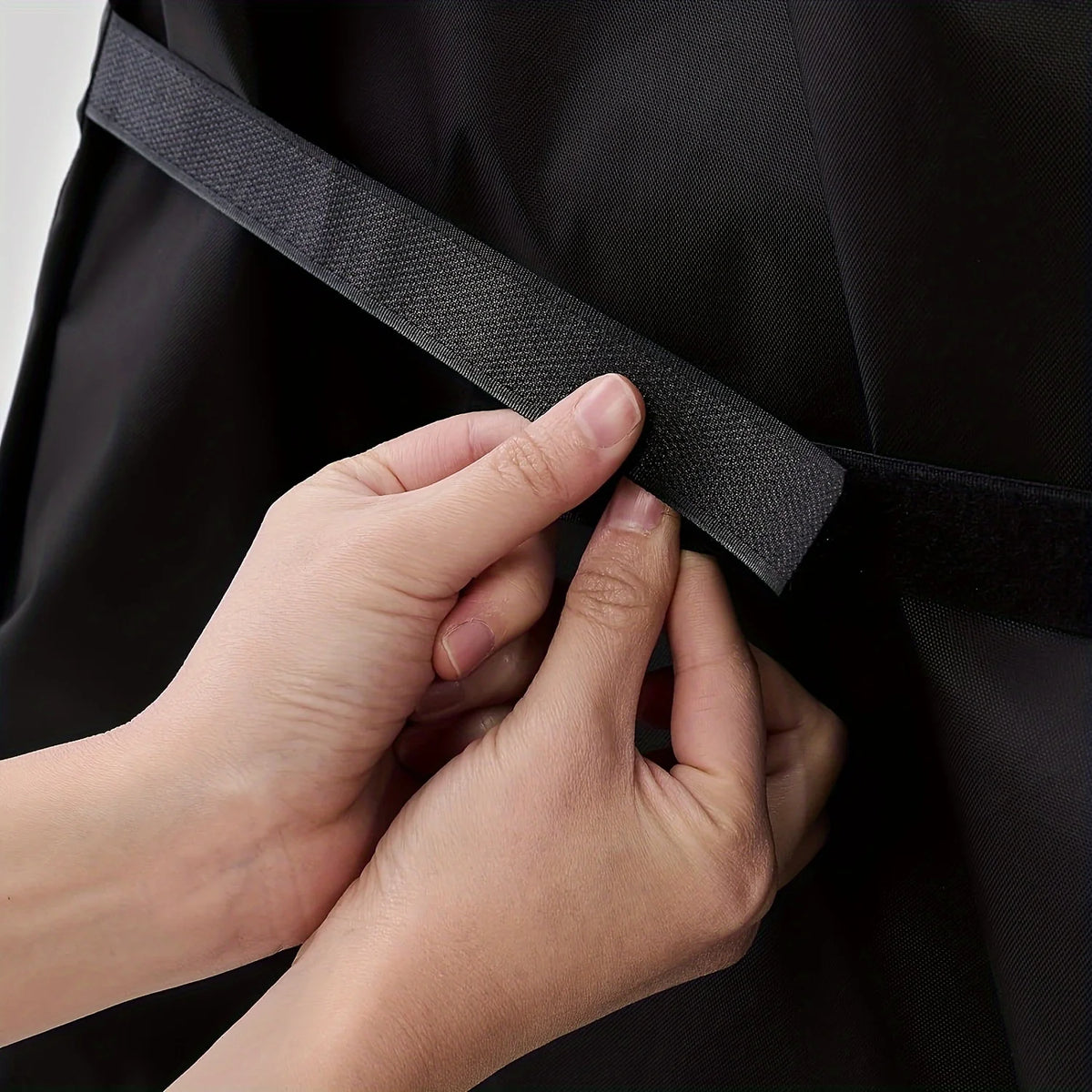 A hand is adjusting the strap of a black heavy-duty waterproof grill cover for a Blackstone.