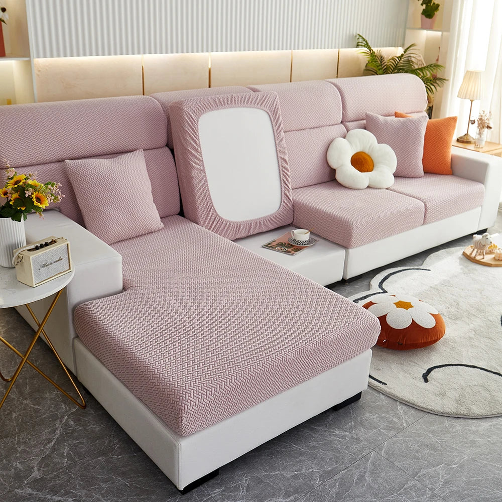 A light pink jacquard elastic sofa slipcover with white cushions and orange accents in a modern living room setting.