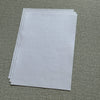 A stack of white water-soluble adhesive embroidery stabilizer sheets lying on a textured green surface.