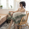 A woman sits in a wicker chair holding a plaid washed cotton pillowcase with ruffled edges.