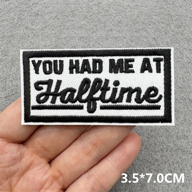 Black and white embroidered patch with the text YOU HAD ME AT Halftime on a gray fabric background