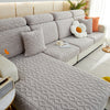 A light gray plush velvet sofa cover with quilted texture and anti-slip backing, featuring orange accent pillows.