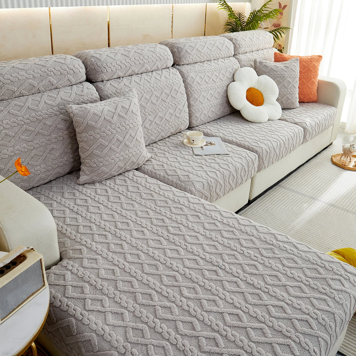 A light gray plush velvet sofa cover with quilted texture and anti-slip backing, featuring orange accent pillows.