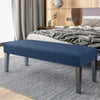 A navy blue velvet bench slipcover with secure straps placed on a gray striped rug in a bedroom setting.