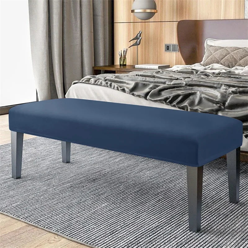 A navy blue velvet bench slipcover with secure straps placed on a gray striped rug in a bedroom setting.