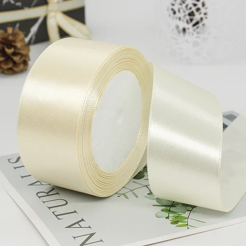 Roll of cream satin ribbon with decorative trim lying on a white surface.