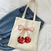 A beige canvas shopping bag featuring a pink bow design with two red cherries on a white background.