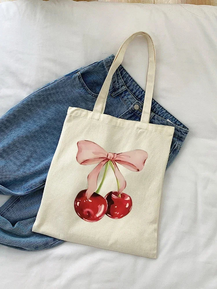 A beige canvas shopping bag featuring a pink bow design with two red cherries on a white background.
