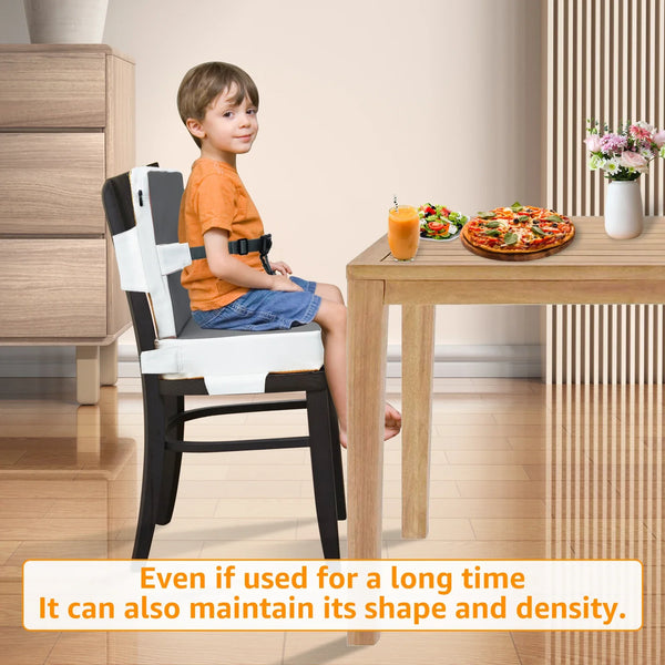 A child is sitting in a black booster seat with a safety belt on a wooden table.