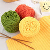 Three balls of soft chenille knitting yarn in green, orange, and yellow resting on a white surface.