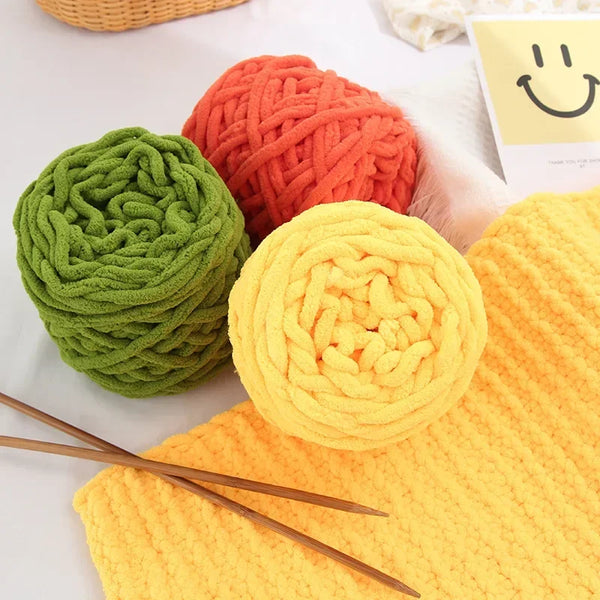 Three balls of soft chenille knitting yarn in green, orange, and yellow resting on a white surface.