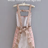 A sleeveless floral pattern kitchen apron in pink and beige fabric hanging on a wooden hanger.
