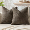 A dark olive green textured pillow resting on a light-colored sofa next to a wooden table.