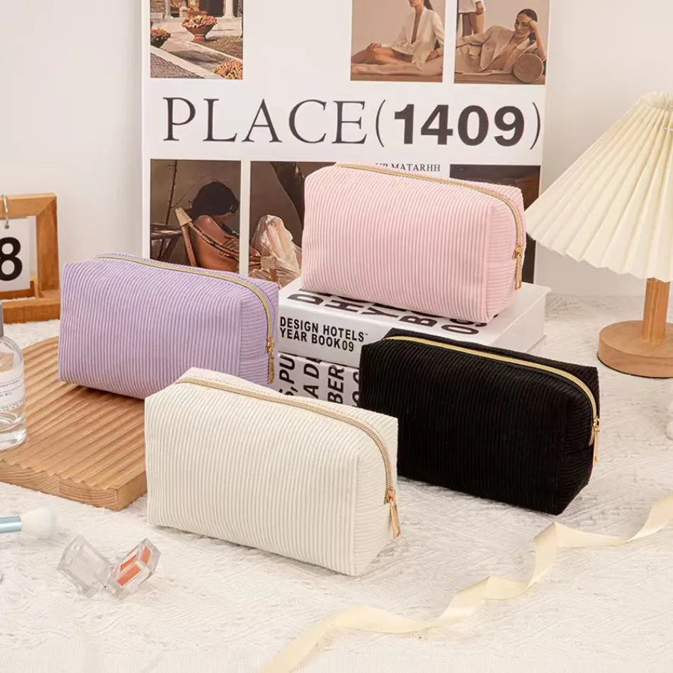 A collection of pink, purple, and black luxury velvet cosmetic storage pouches displayed in front of a sign.