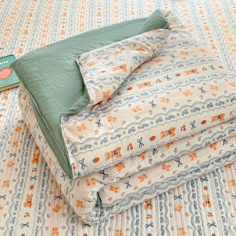 A stack of light blue and orange patterned cartoon quilting comforters lying on a striped fabric background.