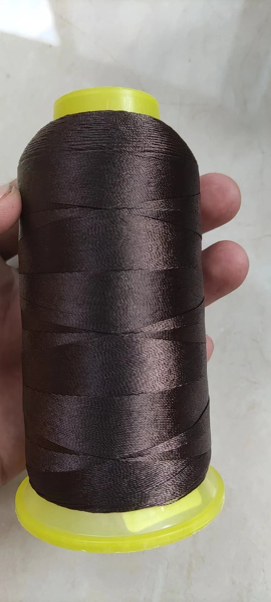 A spool of dark brown high tenacity polyester sewing thread with a yellow plastic core.