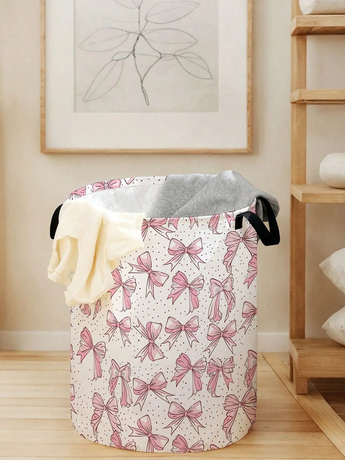 A pink and white canvas laundry basket decorated with a pattern of pink bows, shown on a wooden floor.