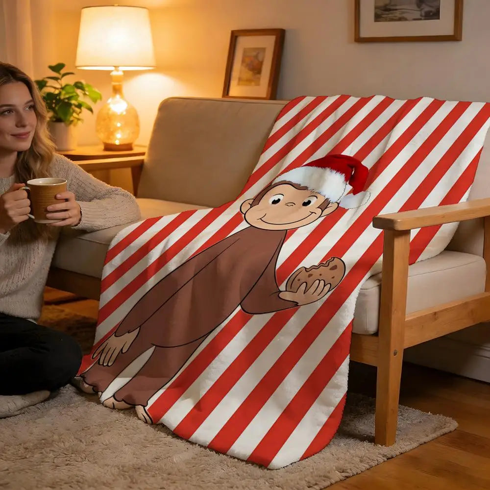 A C-Curious George plush throw blanket featuring the character on a red and white striped fabric draped over a sofa.