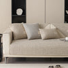 A beige linen sofa cover with several textured cushions on a light-colored sofa in a modern living room setting.