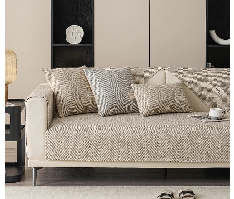 A beige linen sofa cover with several textured cushions on a light-colored sofa in a modern living room setting.