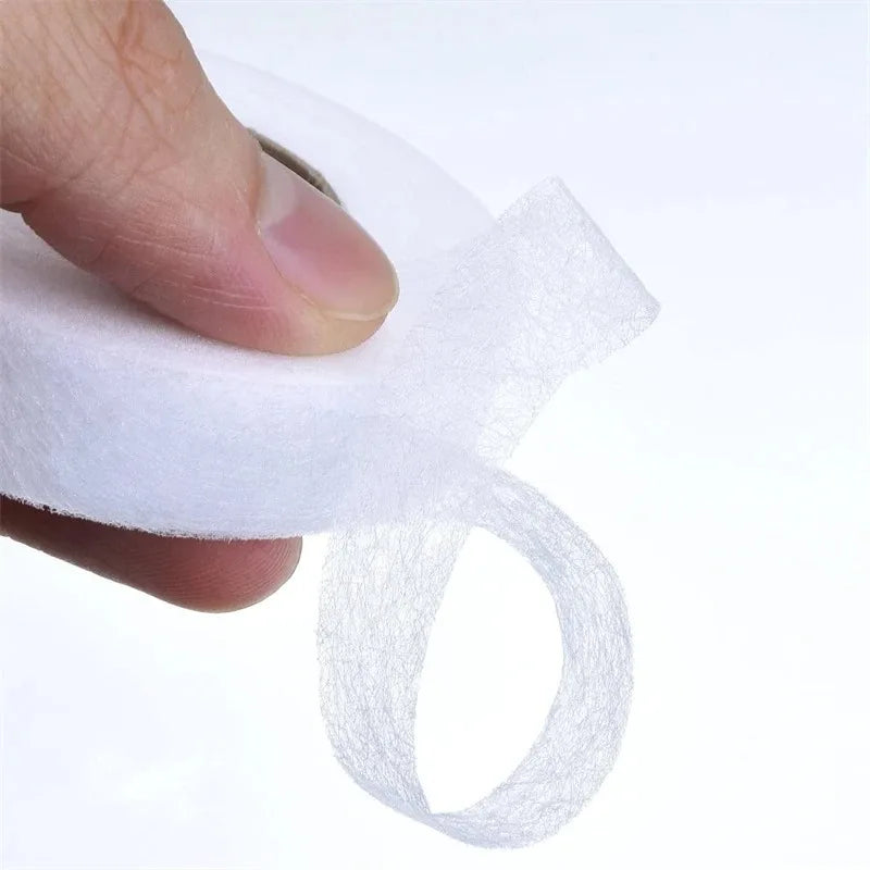 A hand is applying double-sided iron-on adhesive tape for garment repair onto a white fabric.