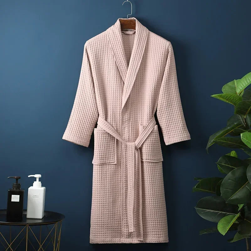 A light pink cotton terry robe hanging on a dark blue wall next to a green plant.