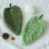 Green textured leaf shaped hand towel resting on white fabric with a seashell and pinecone.