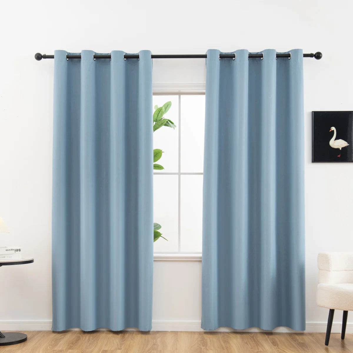 Light blue blackout curtains hanging on a rod in a bright room.