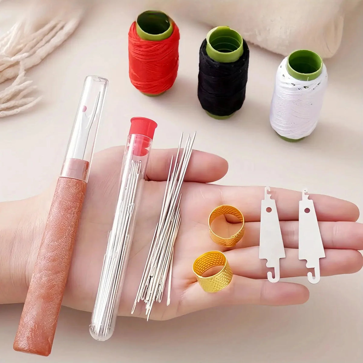 A hand holding a professional hand sewing tool kit featuring red and black thread spools, needles, and gold and white jewelry
