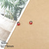A set of two red ladybug resin charms with silver jump rings displayed on brown kraft paper.