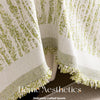 A close-up of an elegant cream and lime green textured fabric blanket with fringed edges.