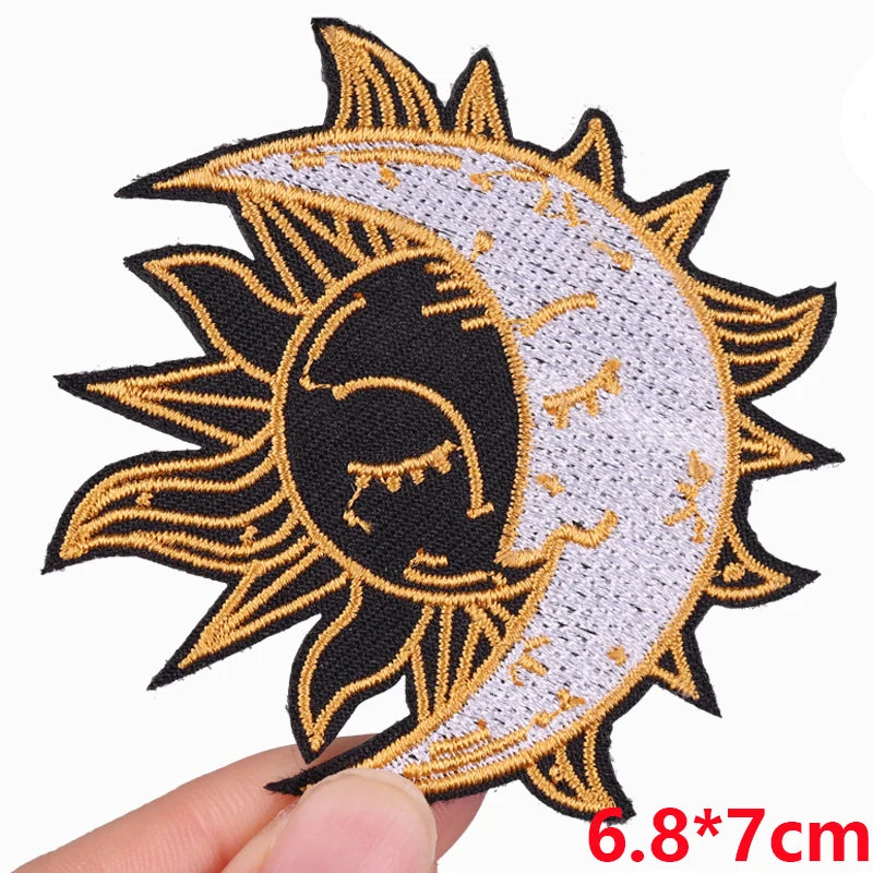 Gold and black embroidered sun and crescent moon patch on a fabric background