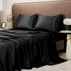 Black luxury solid satin bedding set with pillows draped on a bed against a beige headboard.