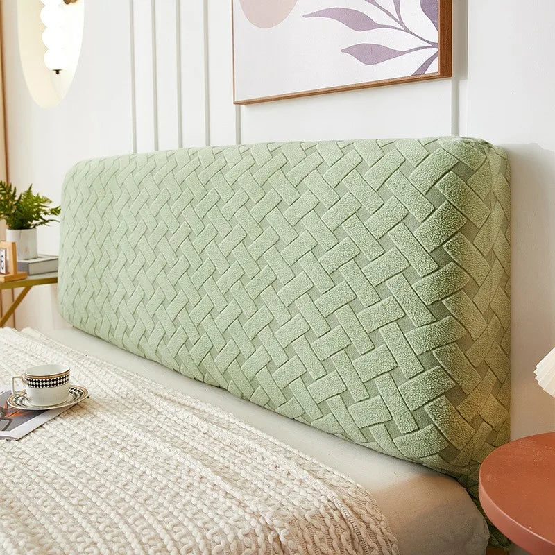 A light green plush quilted headboard cover resting on a bed with a cream textured blanket.