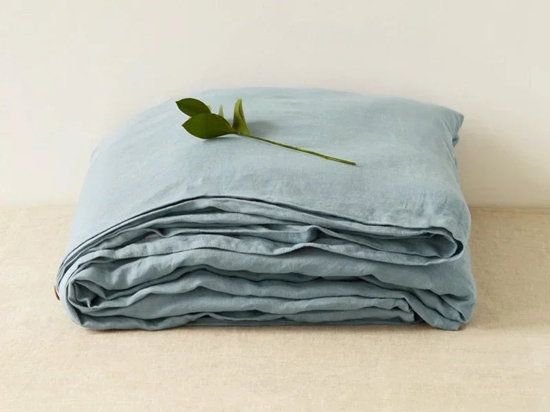 Light blue pure linen flat sheet folded and draped on a light surface with a green leaf.