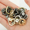 A collection of metal D-shaped ring bag handles and screws in various gold and silver tones held in a hand.
