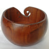 A wooden yarn bowl with a curved lip used for crochet and knitting organization.
