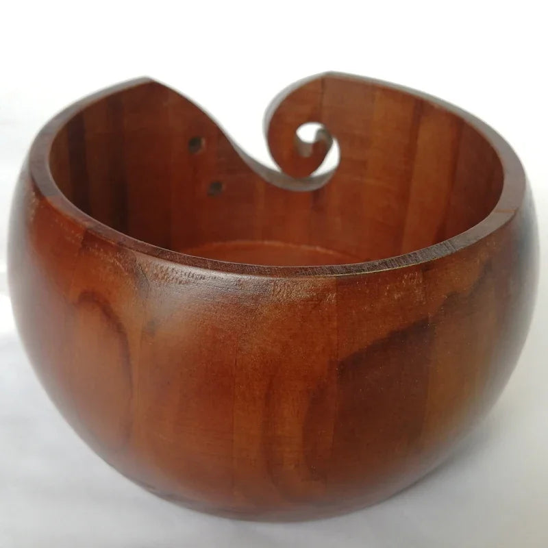 A wooden yarn bowl with a curved lip used for crochet and knitting organization.
