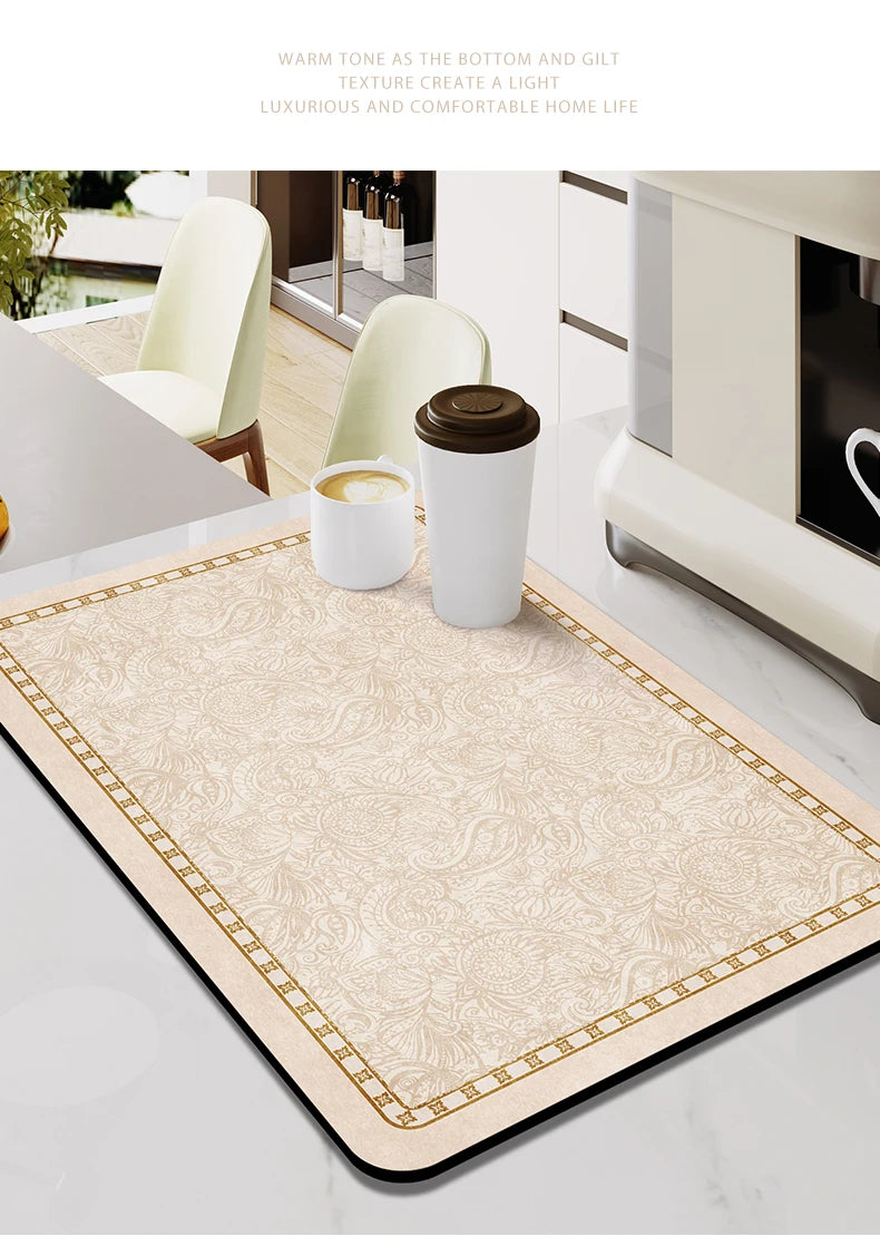 A beige kitchen drain mat with gold trim is shown on a marble countertop next to white cups.