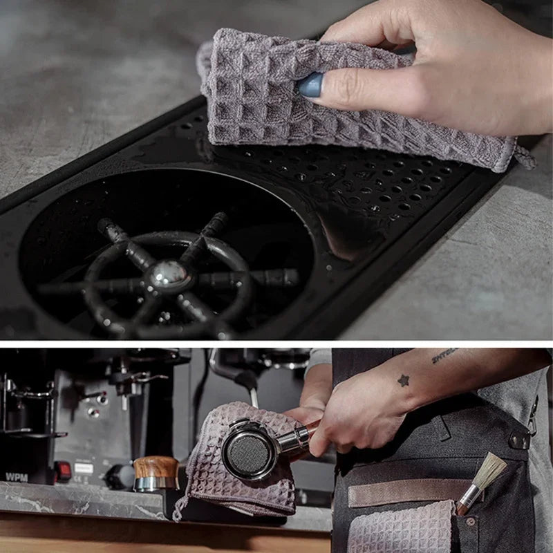 A hand is holding a gray lint-free microfiber cleaning towel over the portafilter of a coffee machine.